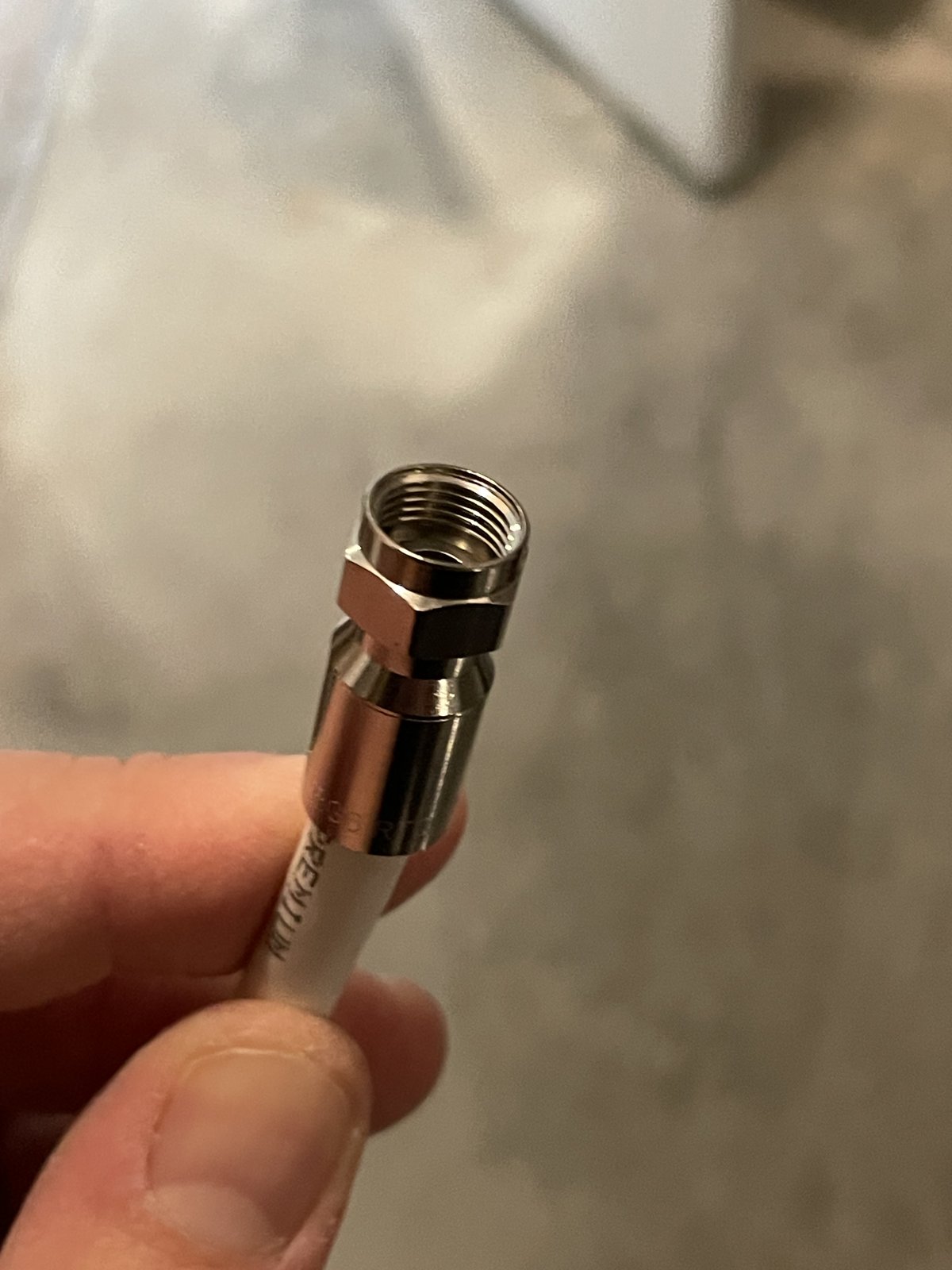 An RG6 coaxial F-connector held between fingers, looking into the barrel, with no copper center conductor protruding