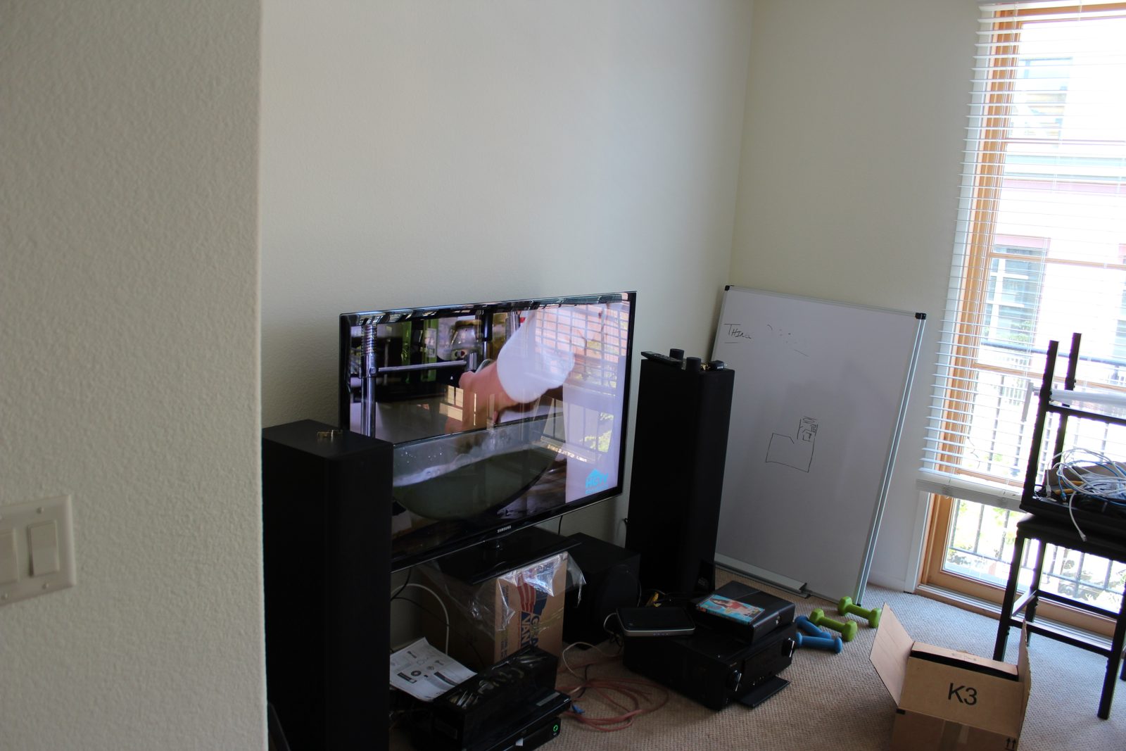 Two black Bowers & Wilkins tower speakers flanking a TV in an apartment, moving boxes still on the floor