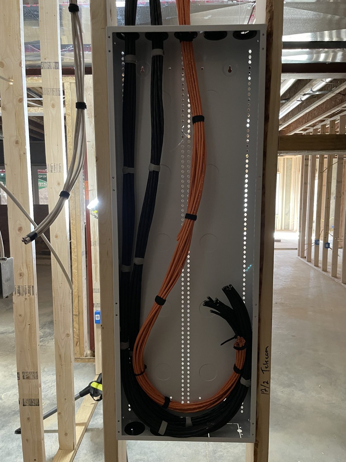 An open stud wall before drywall, with a structured wiring enclosure taking in thick bundles of orange network cable and black cable